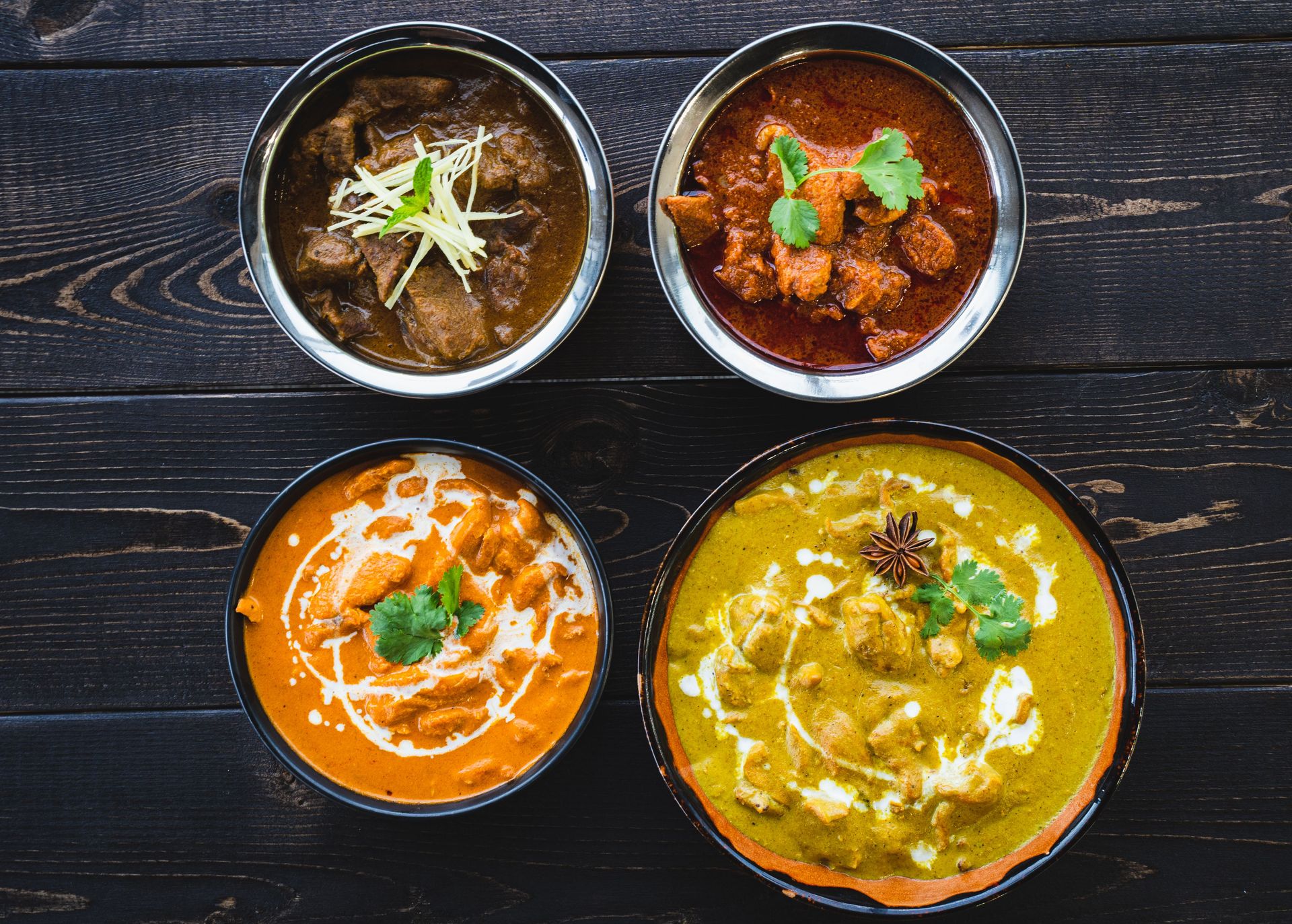 Vibrant Indian curries in bowls on a dark rustic table, ideal for food enthusiasts.